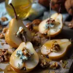 a gourmet preparation of pears, which are halved and elegantly adorned with blue cheese, walnuts, and a drizzle of honey. The pears appear ripe and juicy, carefully sliced to reveal their tender interiors. The blue cheese adds a bold, savory contrast to the sweet fruit, while the walnuts provide a crunchy texture. The honey, visibly dripping over the arrangement, enhances the dish with its golden sweetness. This composition not only highlights the ingredients' natural colors and textures but also suggests a luxurious and flavorful culinary experience.